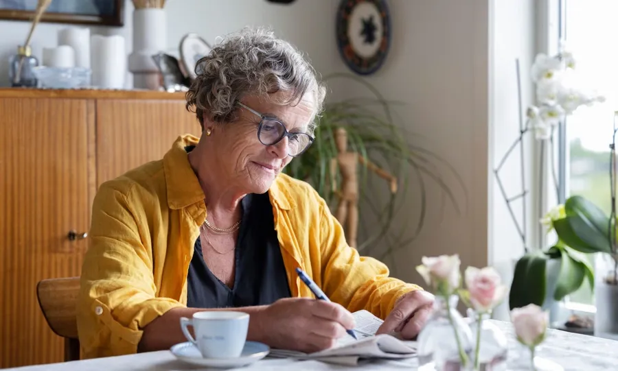 Foto van Gullborg die aan haar tafel zit met een kop koffie en een krant. Blaasproblemen komen vaak voor bij mensen met MS. Meer dan 4 op de 5 mensen met MS krijgen op een bepaald moment in hun leven te maken met incontinentieproblemen. 